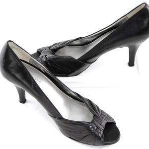 May include: A pair of black leather peep-toe heels. The shoes have a knotted detail on the vamp and a slender, stiletto heel. The interior is silver. These elegant heels are suitable for formal occasions.