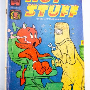 Puede incluir: Un cómic vintage Hot Stuff The Little Devil, número 73, que muestra a un personaje de diablillo rojo sentado en un sillón dental verde mientras una figura con traje protector amarillo y máscara sostiene herramientas dentales.