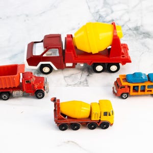 May include: A collection of toy construction vehicles, including a red dump truck, a red cement mixer truck with a yellow drum, a yellow cement mixer truck, and an orange car carrier truck with blue cars.