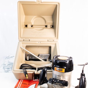 May include: A Craftsman Commercial power router set in a tan carrying case. The router is black and silver with a yellow label. The set includes a manual and various accessories. The case is open, revealing the router and its components.