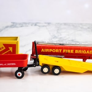 May include: A collection of vintage toy vehicles, including a red Radio Flyer wagon, a yellow Tonka box, and a red Airport Fire Brigade tanker truck. The toys are made of metal and plastic, with black wheels and white accents.