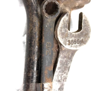 May include: Close-up of a collection of vintage metal tools, including a wrench with the number 35564, a small wrench with "3/8" text, and a socket wrench. The tools are weathered and show signs of use.