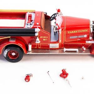 May include: A detailed red and gold model fire engine with the text "Tarrytown" on the side. The model includes a ladder, steering wheel, and accessories. A replica of a vintage fire engine.