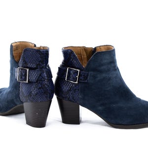 以下が含まれることがあります： ネイビーブルーのスエードアンクルブーツ2足。ブロックヒール。ブーツは、背中と足首に銀色のバックルで固定された、質感のある濃い青色のヘビ柄が特徴です。内側は明るい茶色です。