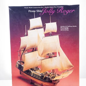 May include: A Lindberg Jolly Roger pirate ship plastic model construction kit box. The box features an illustration of a tall ship with beige sails and a dark hull, with text stating 16 Inches Long and Detailed Crew Members.