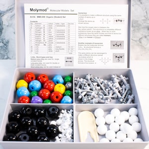 May include: A Molymod molecular models set for organic chemistry students. The set includes colored spheres representing atoms, gray links, and a white tray. The box contains instructions and diagrams for building molecular structures.