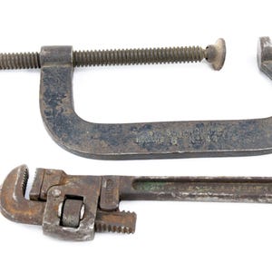 May include: Two vintage metal tools on a white background. A large C-clamp with a screw mechanism and a small adjustable wrench are displayed. The C-clamp has the text "SUPER CLAMP" and "HACKSAW 6 N-44".