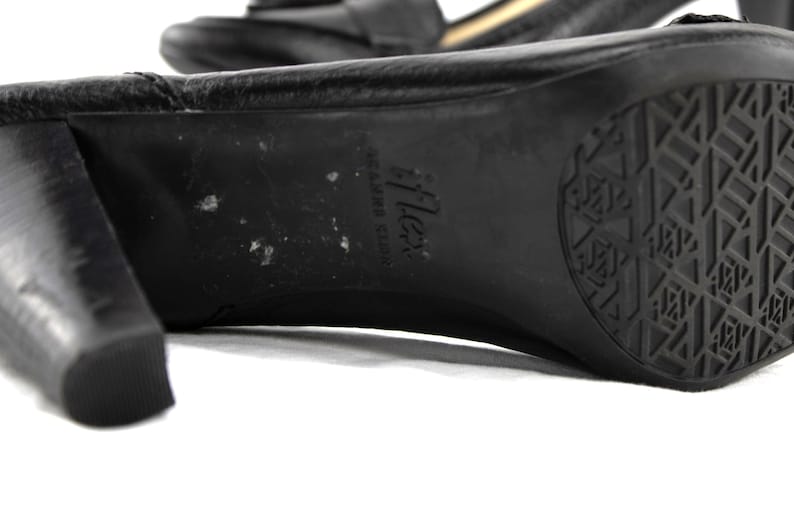 May include: Close-up of a black leather heeled shoe. The sole features a textured pattern and the brand name "iFlex". The heel is thick and square. The shoe is on a white background.