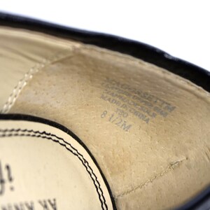 May include: Close-up of the interior of a black shoe. The insole is beige with text that includes the size 8 1/2M. The shoe's edge is black with a stitched design.
