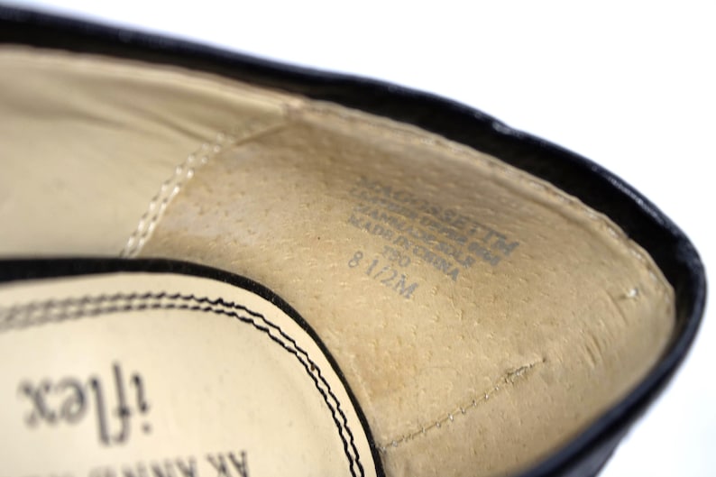 May include: Close-up of the interior of a black shoe. The insole is beige with text that includes the size 8 1/2M. The shoe's edge is black with a stitched design.