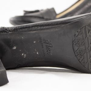 May include: Close-up of a pair of black leather heeled shoes. The sole of the shoe is visible, featuring a textured pattern and the brand name "flex". The heel is thick and sturdy. The other shoe is slightly out of focus in the background.