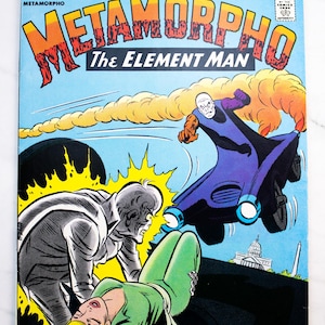 Könnte beinhalten: Ein klassisches DC-Comicbuch mit dem Titel 1st Issue Special, das Metamorpho The Element Man zeigt. Das Cover zeigt eine Figur in einem violetten Anzug, die ein Fahrzeug steuert, eine graue Figur und eine blonde Person am Boden.