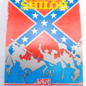May include: A vintage board game box titled "The Battle of Shiloh." The box features a Confederate flag design in red, white, and blue, with illustrations of soldiers and cannons. The game is a historical simulation.
