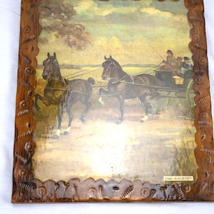 May include: An antique framed print depicting a horse-drawn carriage with passengers. The artwork features two dark horses pulling the carriage across a field. The frame is made of dark wood with a carved design. The text "THE HACKNEY" is visible.