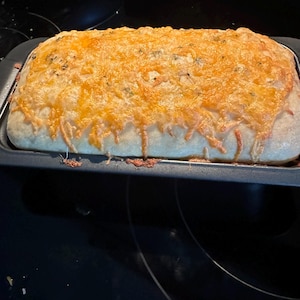 May include: A loaf of bread topped with melted cheese in a loaf pan. The bread is golden brown and the cheese is melted and bubbly.