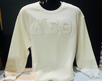 May include: White long-sleeve sweatshirt with a large embroidered white Greek letter design that reads "ΔΣΘ".