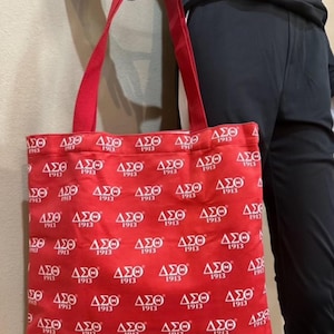 May include: A red tote bag with white  "ΔΣΘ 1913"  logos repeated all over the bag. The bag has two red handles.