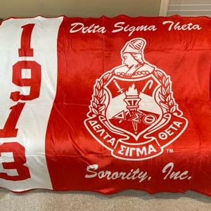May include: Red and white fleece blanket with the Delta Sigma Theta Sorority, Inc. logo and the year 1913. The logo features a white crest with a torch, a crown, and the letters "Delta Sigma Theta" in a circle.