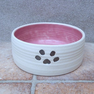May include: White ceramic pet bowl with a pink interior and a paw print design.