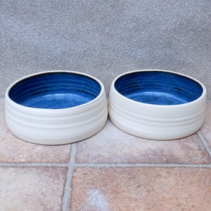 May include: Two white ceramic bowls with a blue glaze inside. The bowls have a textured, ridged exterior.