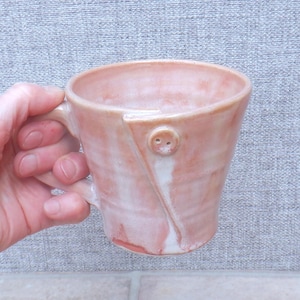 Taza de café/té hecha a mano de cerámica de gres con detalle de botón y esmalte rosa coral.