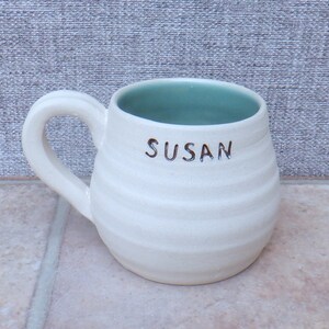 May include: White ceramic mug with a light green interior and the name "SUSAN" written on the front.