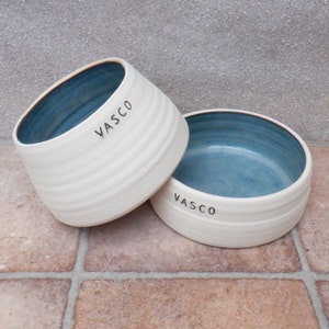 May include: Two white ceramic bowls with blue interiors. Both bowls have the name "VASCO" inscribed on the outside.