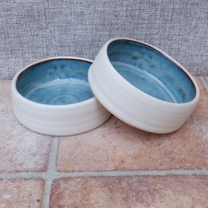 May include: Two white ceramic bowls with a blue glaze inside. The bowls have a brown rim.