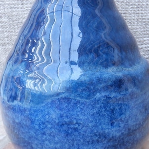 May include: A ceramic vase with a glossy, undulating surface featuring a deep blue glaze. The finish transitions from a lighter, reflective cobalt blue at the top to a darker, textured navy blue at the base, creating a rich, layered appearance.