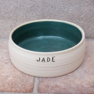Puede incluir: Tazón de cerámica blanco para mascotas con interior verde y el nombre "JADE" escrito en la parte delantera.