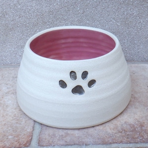 Puede incluir: Tazón de cerámica blanco para mascotas con interior rosa y diseño de huella de pata gris.