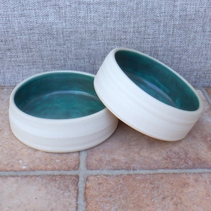 May include: Two white ceramic bowls with a teal green interior. The bowls are stacked on top of each other.