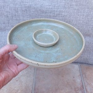 May include: A handmade ceramic serving platter with a light green glaze. The platter has a circular shape with a raised rim and a smaller, matching bowl in the centre. The speckled surface adds a rustic touch to this functional piece.