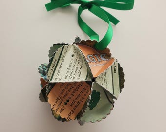 May include: A green ribbon tied into a bow hangs from a green and white paper ornament. The ornament is made from folded Magic: The Gathering cards. The text on the cards reads "Ant-Arcane", "Aura", "Flashback 6", "You may return this card from your graveyard to your hand. Then return it to the battlefield. It's flashback cost is equal to its mana cost.", "Put a 3/3 green Elephant token into play.", "Ret creature gets +2/+2.", "When this creature enters the battlefield, you may return target Aura from your graveyard to your hand and put it onto Arcane (A).", "Magic: The Gathering", "De Gather", "3 life."