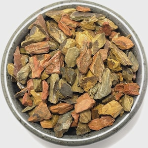 May include: A gray ceramic bowl filled with colorful, irregularly shaped rocks. The rocks display a variety of colors, including shades of red, orange, yellow, and green. The bowl's rim is a darker gray, providing a contrast to the vibrant stones.