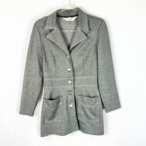 May include: A gray blazer with white stitching details. The blazer has a notched collar, three buttons, and two front pockets. The stitching outlines the collar, pockets, and waistline. The blazer is hanging on a clear hanger.