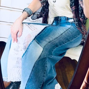 May include: Patchwork denim jeans in shades of light, medium, and dark blue, featuring a wide leg and a raw hem. The model is wearing a white top and a patterned kimono. The jeans are a stylish, casual garment.