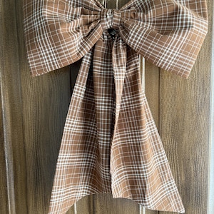 May include: A large, decorative bow made of brown fabric with a white plaid pattern. The bow is tied in the center and has long, flowing tails. The bow is hanging on a door.