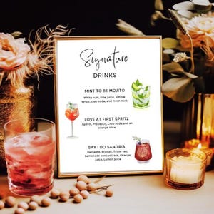 May include: A white sign with black text that reads "Signature Drinks". The sign lists three signature drinks with their ingredients: "Mint to Be Mojito", "Love at First Spritz", and "Say I Do Sangria".