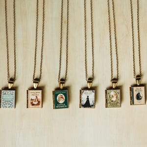 May include: Six gold-toned metal chain necklaces, each featuring a miniature rectangular book pendant. The pendants display classic book covers including Sense and Sensibility, Little House on the Prairie, Little Women, Pride and Prejudice, Anne of Green Gables, and Black Beauty.