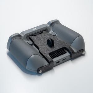 Puede incluir: Un controlador de dron gris con empuñaduras negras texturizadas y un soporte de montaje negro texturizado. El controlador tiene una pantalla integrada y varios botones. El logotipo de DJI es visible en la parte superior.