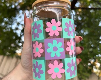 May include: A clear glass jar with a bamboo lid and a retro floral design. The design features pink and purple flowers on a green and purple checkered background.