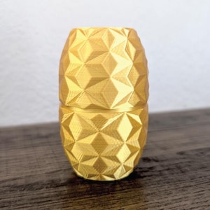 May include: A gold-colored, geometrically patterned, cylindrical container with a lid. The container is made of a smooth, shiny material.