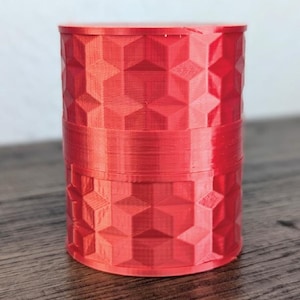 Op de afbeelding: Een rode cilindrische container met een geometrisch patroon. De container is gemaakt van een 3D-geprint materiaal.