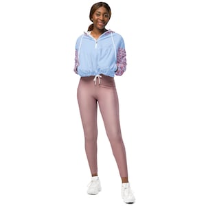 Könnte beinhalten: Eine Frau trägt eine hellblaue Jacke mit rosa Blumenärmeln und einem Kordelzug in der Taille. Sie trägt auch mauvefarbene Leggings und weiße Turnschuhe. Das Outfit ist sportlich und lässig.