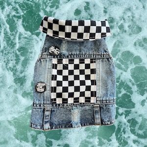 May include: A denim dog vest with a black and white checkered collar and pocket. The vest has patches that say "Punk Pet" and "Jimmy Eat World". The vest is distressed with a ripped section.