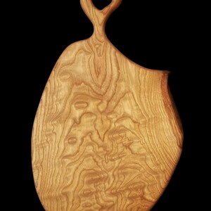 May include: A large, wooden cutting board with a unique, organic shape and a handle with a hole in the center. The board has a natural wood finish and a beautiful grain pattern.