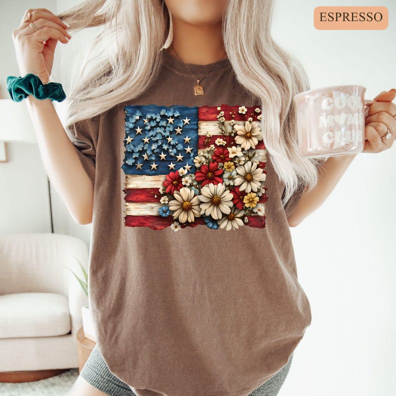 May include: Espresso-colored t-shirt featuring a distressed American flag design. The flag's stars are replaced with blue flowers, and the stripes are adorned with red, white, and yellow flowers. The shirt has a relaxed fit.