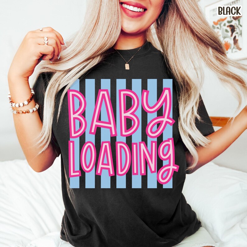 May include: Black t-shirt with the text "BABY LOADING" in pink letters over a light blue striped background. The shirt is a crew neck style.
