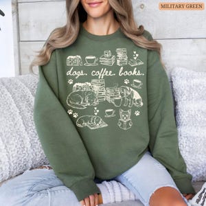 May include: Military green sweatshirt with a white graphic design featuring dogs, books, coffee cups, and the text "dogs. coffee. books." The design includes paw prints and illustrations of dogs reading.